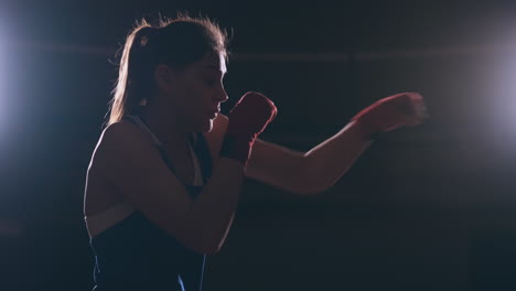 A-beautiful-sports-boxer-woman-in-red-bandages-on-her-hands-and-a-blue-t-shirt-is-fighting-with-a-shadow-practicing-the-speed-and-technique-of-punches.-Camera-movement-side-View.-Steadicam-shot.-Preparing-for-self-defense