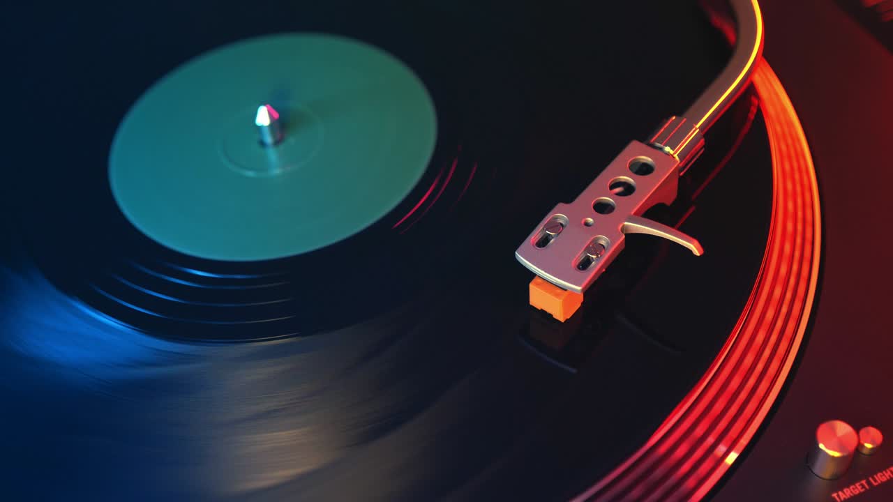 초점을 맞추지 않는 플레이어 비닐 레코드 턴테이블 빨간색과 파란색 불빛의 배경에서 근접. 바늘은 회전하는 검은 비닐 레코드에서 부드럽게 슬라이드