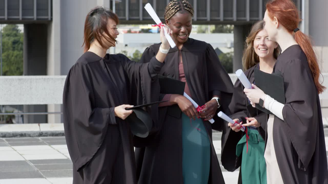 Un laureato che alza il diploma induce le laureate ad aggiustarsi i cappelli e a esultare nel cortile.