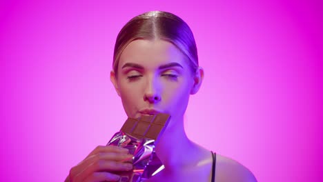 gorgeous woman in two light studio background takes a bite of chocolate bar