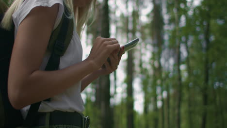 primer plano de una mujer con un teléfono móvil caminando por el bosque viajando con una mochila en cámara lenta. navegar por el bosque usando el navegador en su teléfono móvil