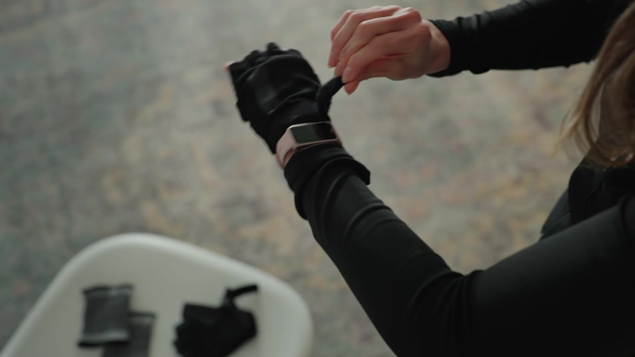 Focused woman securing her glove strap. Female preparing her glove with concentration before physical exercise. Closeup image of woman adjusting her gloves carefully prior to workout session