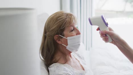 mujer mayor con máscara facial midiendo su temperatura en casa