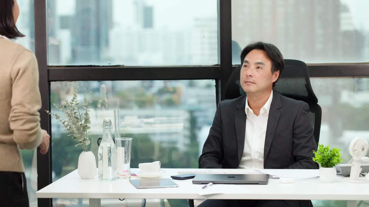 Manager and employee exchange handshake and documents in bright, modern office with city view