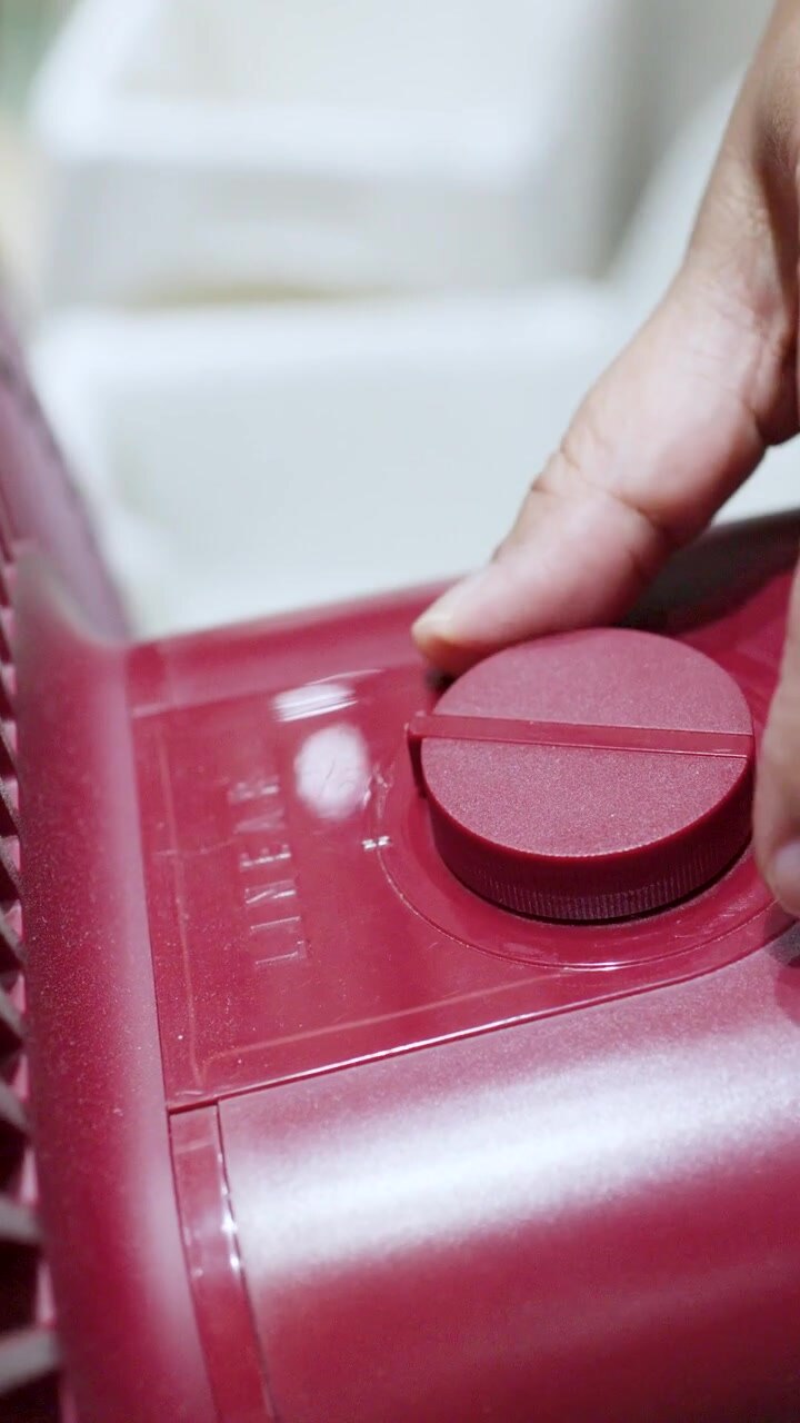 A close-up shot shows a hand adjusting the dial knob on a red electric fan.