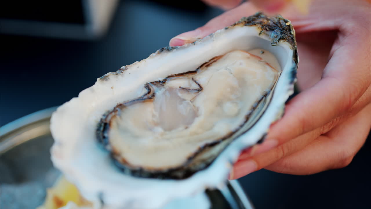 Woman pouring lemon juice on a raw oyster at a restaurant