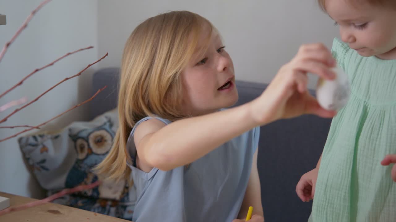Young Girl Decorating Easter Egg and Showing it to Her Sister