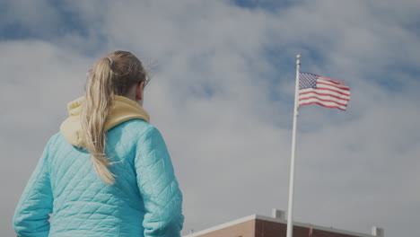 Kind-Im-Schulpflichtigen-Alter-Blickt-Auf-Die-US-Flagge-Am-Fahnenmast,-Rückansicht