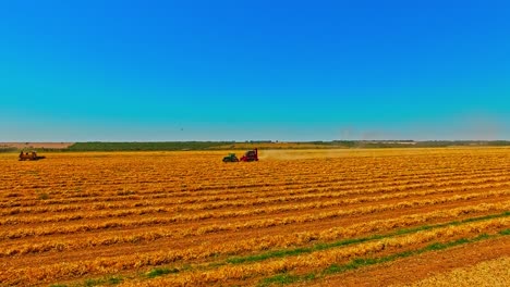 flying towards three tractors working in a dry field on a hot day, drone shot