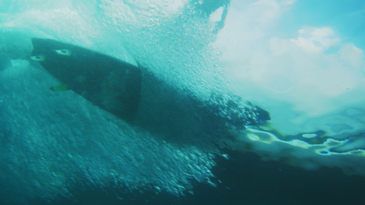 Surfer carves above shallow reef, rearview underwater in slow motion