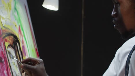 primer plano de un artista masculino afroamericano pintando con un cuchillo de paleta en un lienzo en un estudio de arte