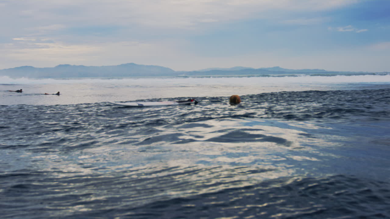 Slow motion view of surfer in water holding surfboard at Cloudbreak Fiji turning to paddle out