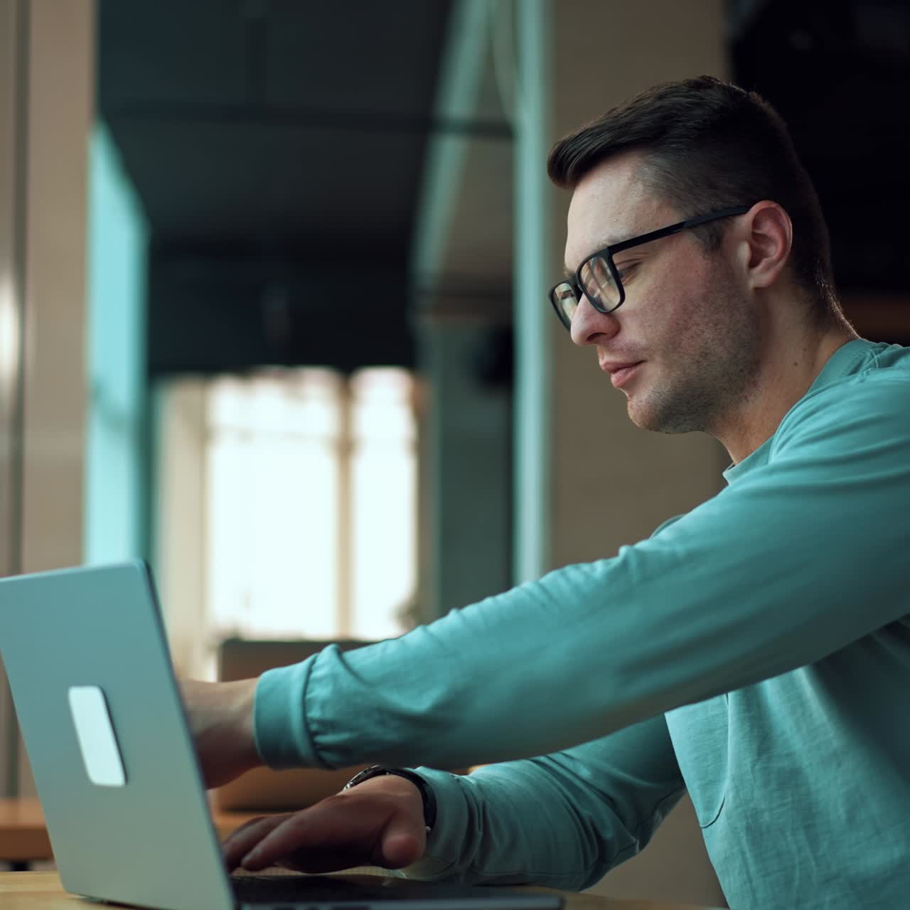 Man working on laptop and drinking coffee from a paper cup. Positive smiling businessman typing on computer sitting in comfortable office