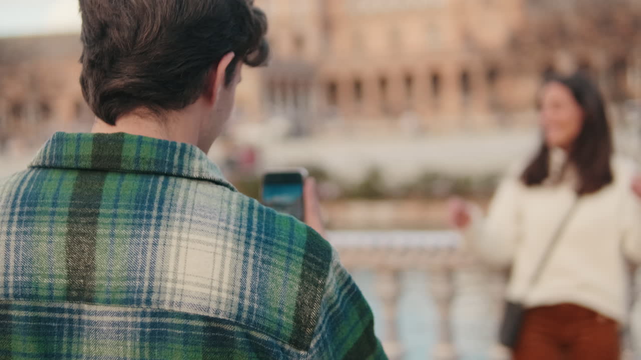 Young man taking photo of his girlfriend on mobile phone, focus on man