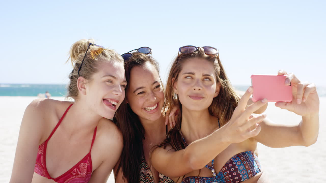 세 명의 십대 여자 친구들이 해변에서 셀피를 찍고 화려한 비키니를 입고 휴가 사진을 공유하고 있습니다.