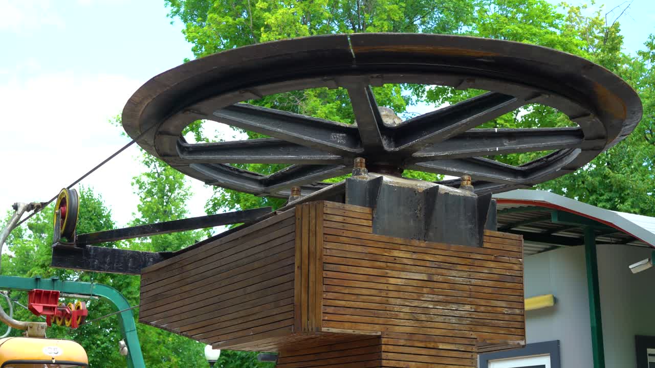 большое металлическое колесо канатной дороги вращается горизонтально в городском парке летом