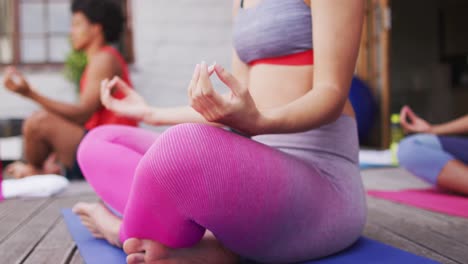 Midsection-of-biracial-woman-practicing-yoga-with-group-of-diverse-friends-in-backyard