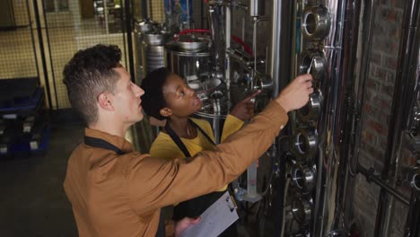 diverse male and female colleague at gin distillery inspecting equipment and discussing