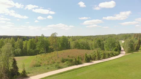 drone flying up above northern european landscape with country road near vast forest, sunny summer day