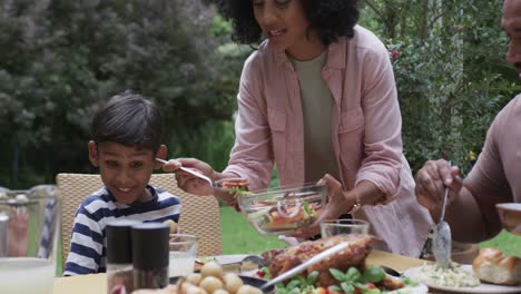 Happy-biracial-parents,-son-and-daughter-enjoying-meal-at-dinner-table-in-garden,-slow-motion