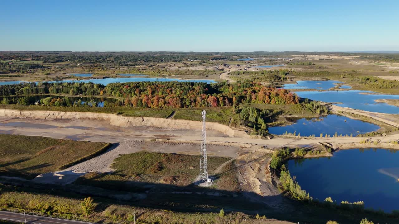 A stunning aerial view of a telecommunications tower in a Caledon, Ontario gravel pit, surrounded by beautiful blue quarry lakes and a forest with vibrant autumn colours