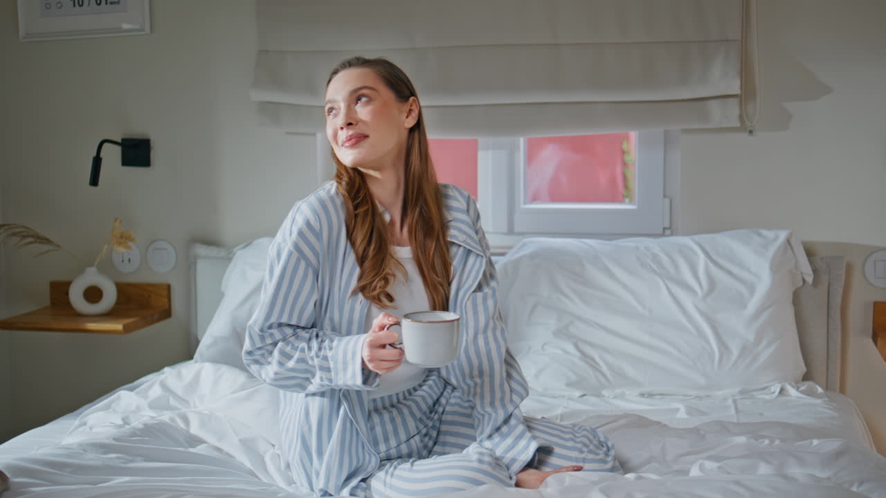 Carefree lady relaxing bedroom savoring coffee with gentle smile. Relaxed woman