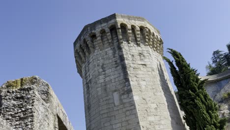 Huge-hexagonal-stone-tower-in-front-of-a-blue-sky-made-of-light-stone-with-a-stone-wall-in-the-foreground-on-a-rough-rock-in-good-weather-in-Europe