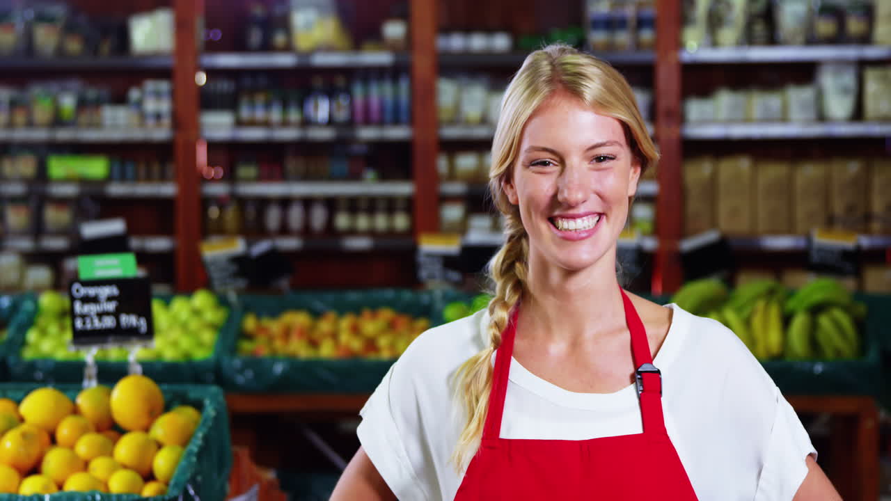 Smiling female staff standing with hands on hip in grocery section