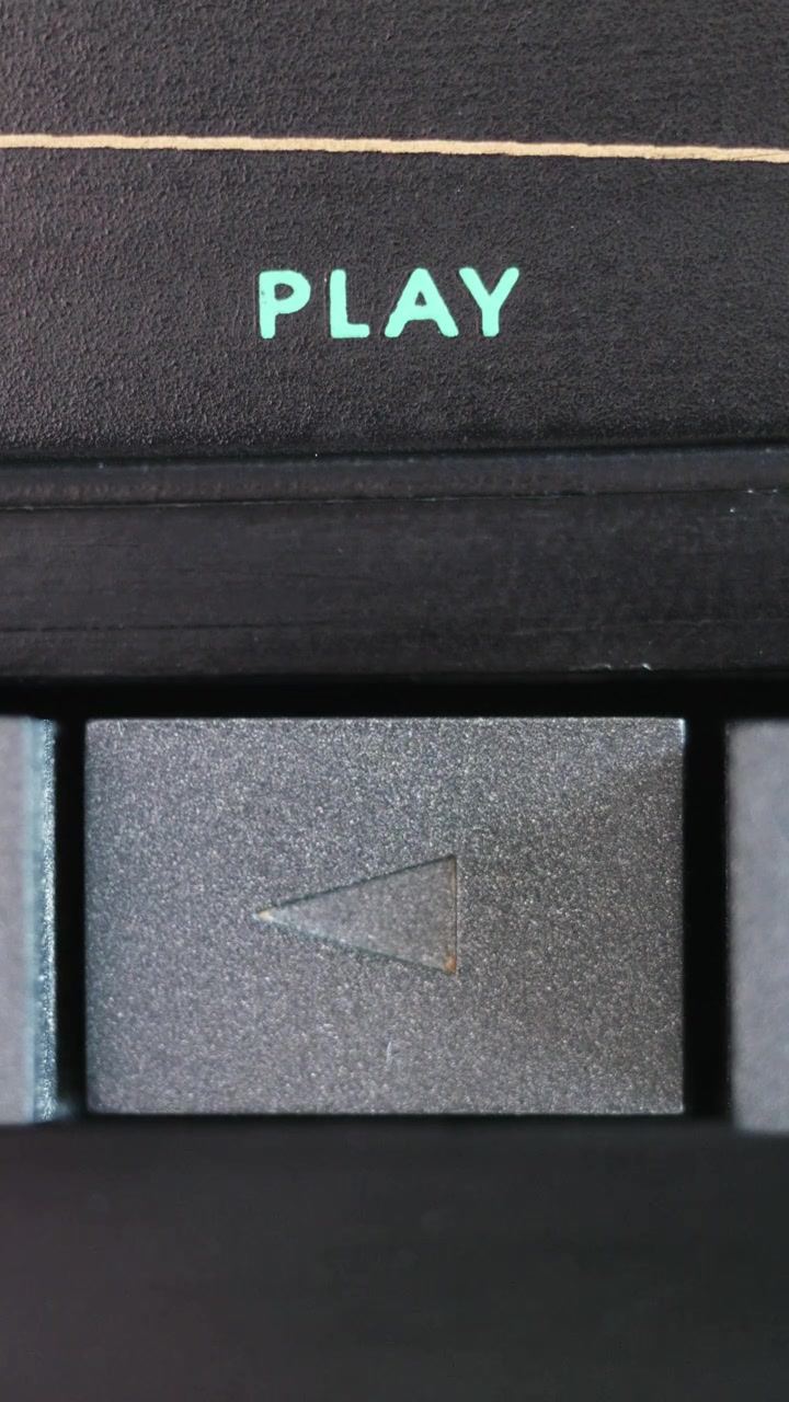 Vertical macro shot of gray play button being pressed below turquoise text on black panel