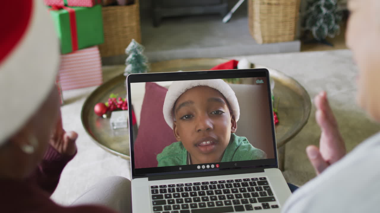 diversas amigas mayores agitando y usando una computadora portátil para una videollamada de navidad con un niño en la pantalla