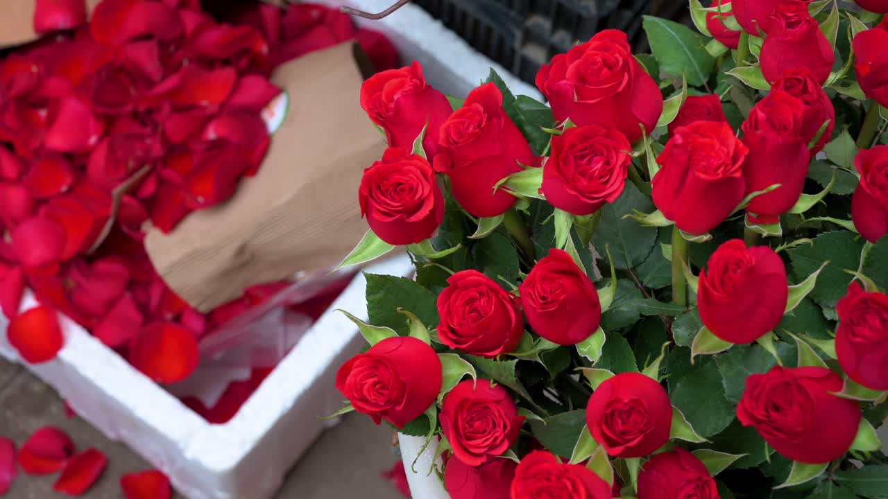 se ve una boutique de rosas a la venta en un mercado de flores mientras se ven pétalos de rosas rojas en el suelo durante el día de san valentín