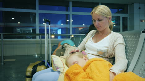 a woman is stroking a girl sleeping on her lap sitting in the terminal of the airport flight delay c