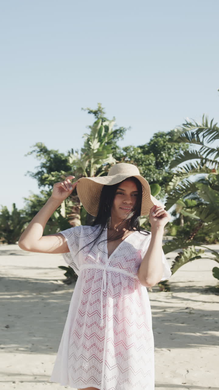 Vertical video portrait of happy biracial woman in sunhat and sundress on sunny beach, slow motion