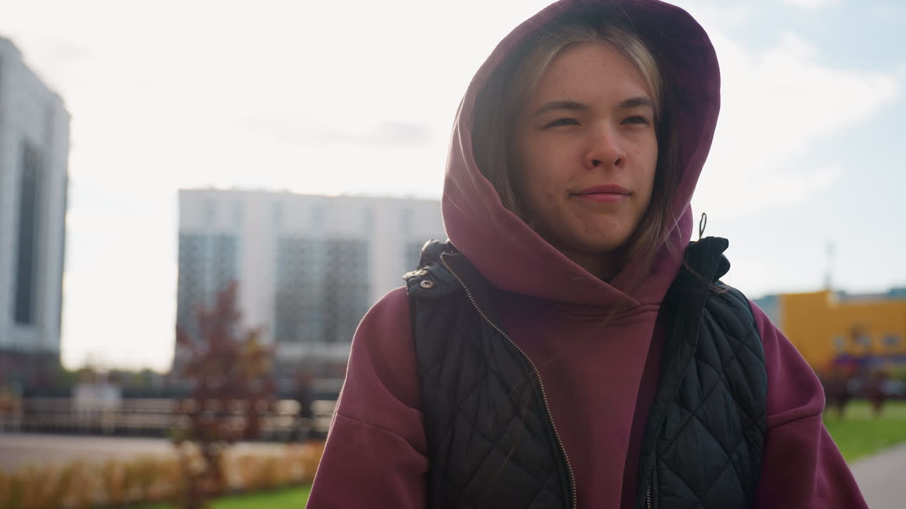 Medium shot of student in sports wear jumping during warm up exercise with excitement on her face outdoor under bright sun amid flowers shrubs and tall urban buildings in background