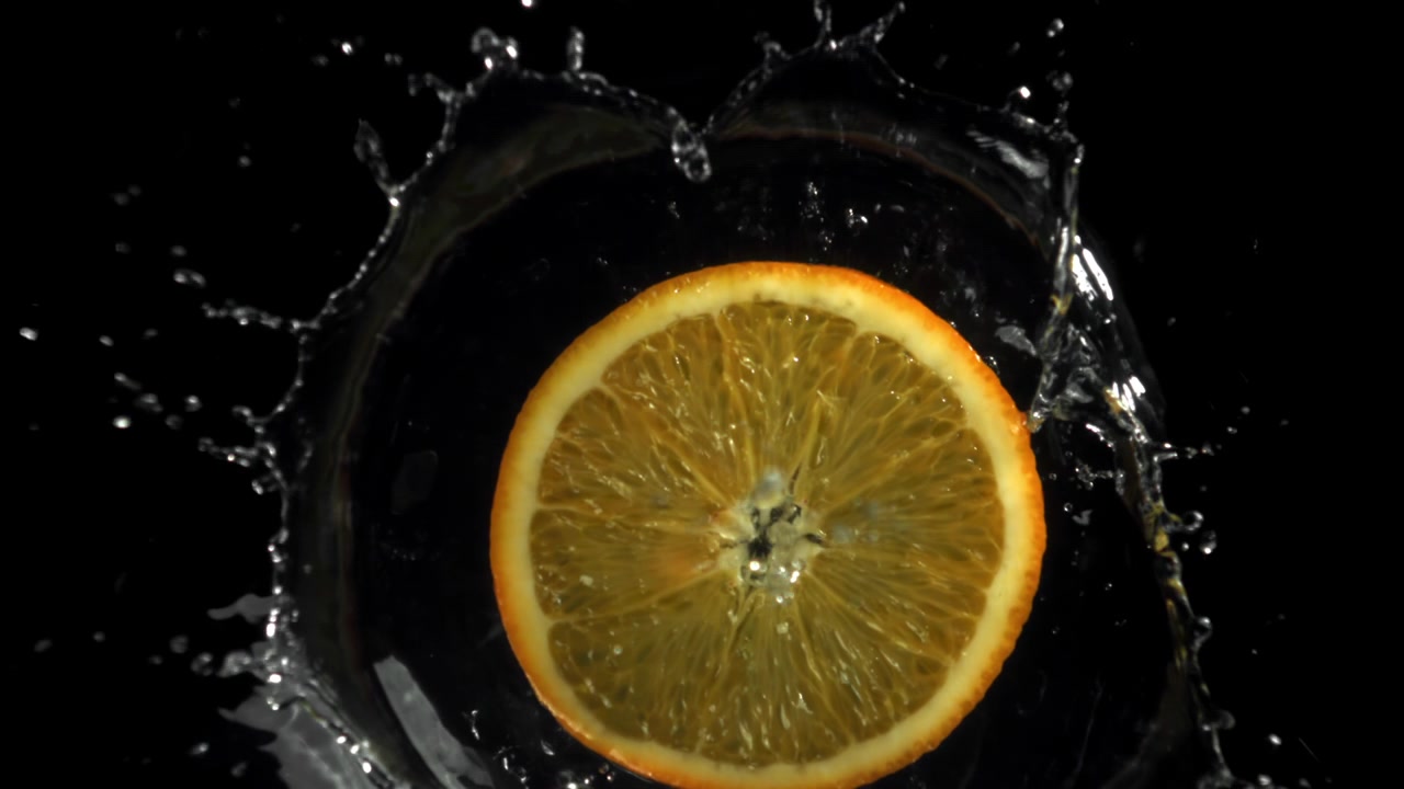 Schizzi d'acqua al rallentatore su una fetta d'arancia fresca su sfondo nero