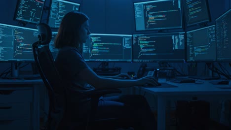 a focused programmer engaged in coding tasks surrounded by multiple monitors displaying lines of code in a dimly lit workspace
