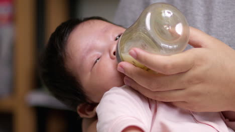 slow motion close-up of 2-month-old baby girl drinking milk from a bottle while being fed by her mother