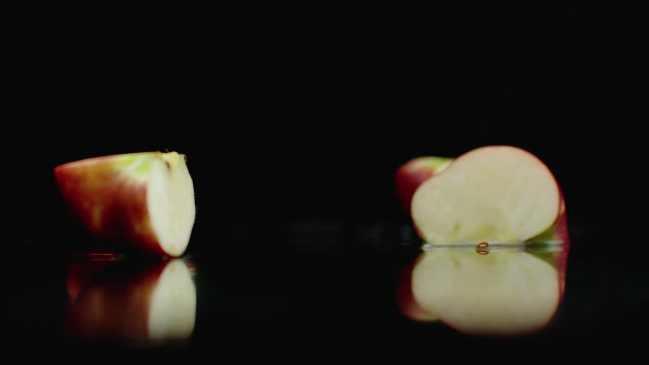 Red juicy sliced ​​apple falling on a glass with splashes of water in slow motion on a dark background