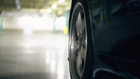 close-black-car-wheel-drives-on-gray-asphalt-on-parking-lot