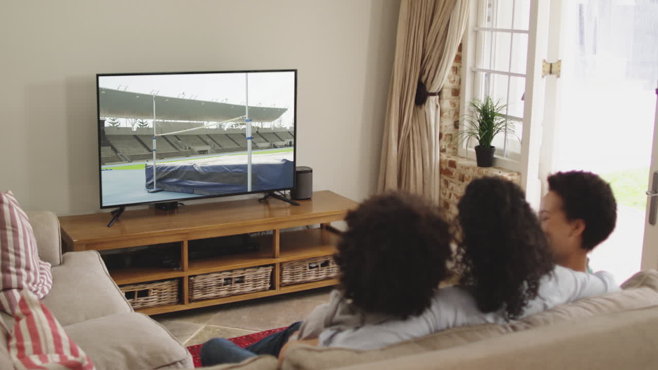 Famiglia felice seduta a casa insieme che guarda l'atletica salto in alto in TV