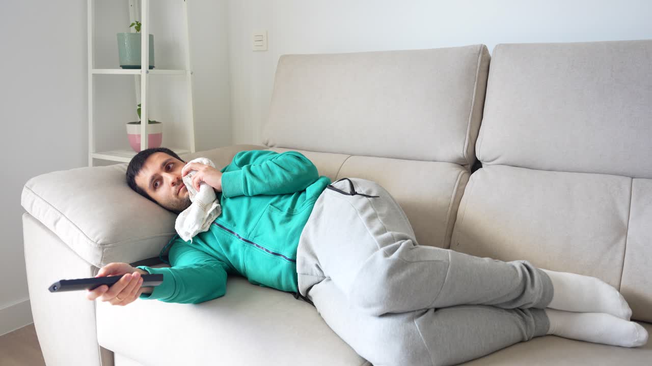 adulto con dolor en la boca aplicando hielo mientras se ríe de la tv