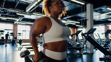plus-size woman working out with dumbbells in gym