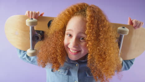 fotografía de estudio de una joven con una patineta en los hombros contra un fondo púrpura