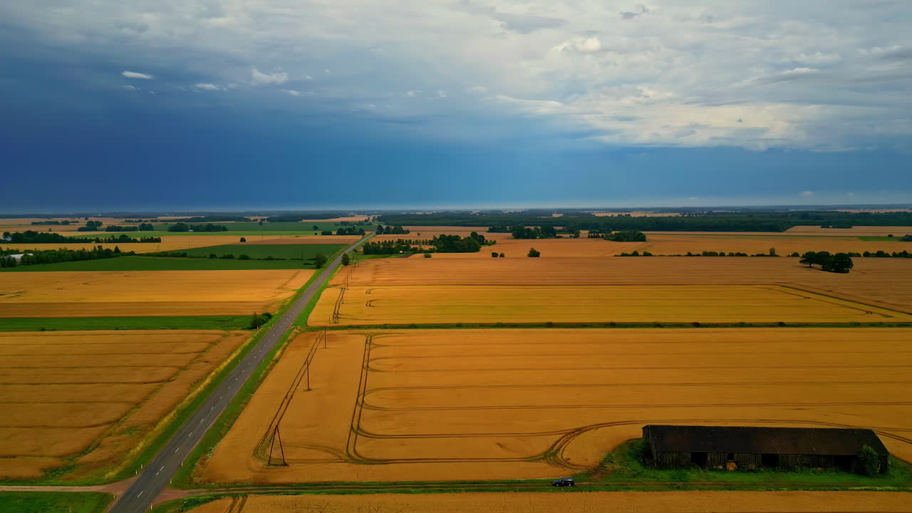 Drone shot of agricultural green and light brown fields on a cloudy day, with a coming storm on the background