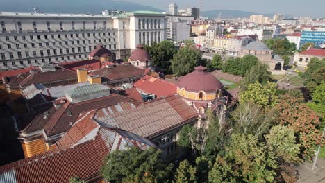 aerial rising beside trees to reveal sofia cityscape views in bulgaria, banya bashi mosque and regional history museum