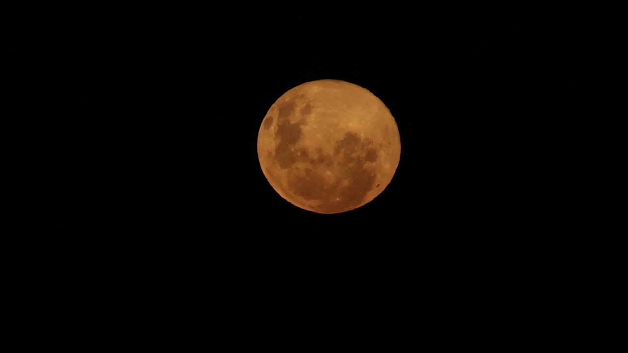 Lua cheia vermelha detalhada surge lentamente no céu noturno com espaço em preto para texto