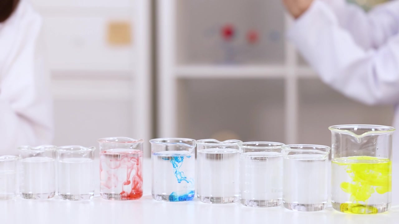 Elever i hvide laboratoriekittel blander farverige farvestoffer i glaskolber under et naturvidenskabeligt eksperiment i skolen