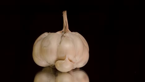 slowly spinning garlic bulb reveals individual cloves in cinematic closeup as each segment comes into focus against black background and mirror surface