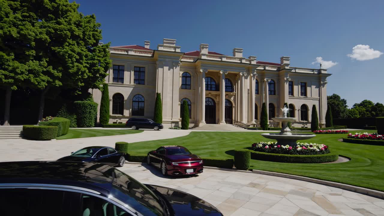 Aerial video view of a luxurious mansion with manicured gardens and elegant cars
