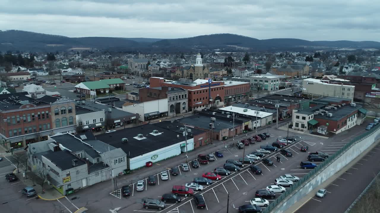 A circular drone shot of a small Midwestern town with a chapel and rolling hills in the background and a quiet street in the foreground
